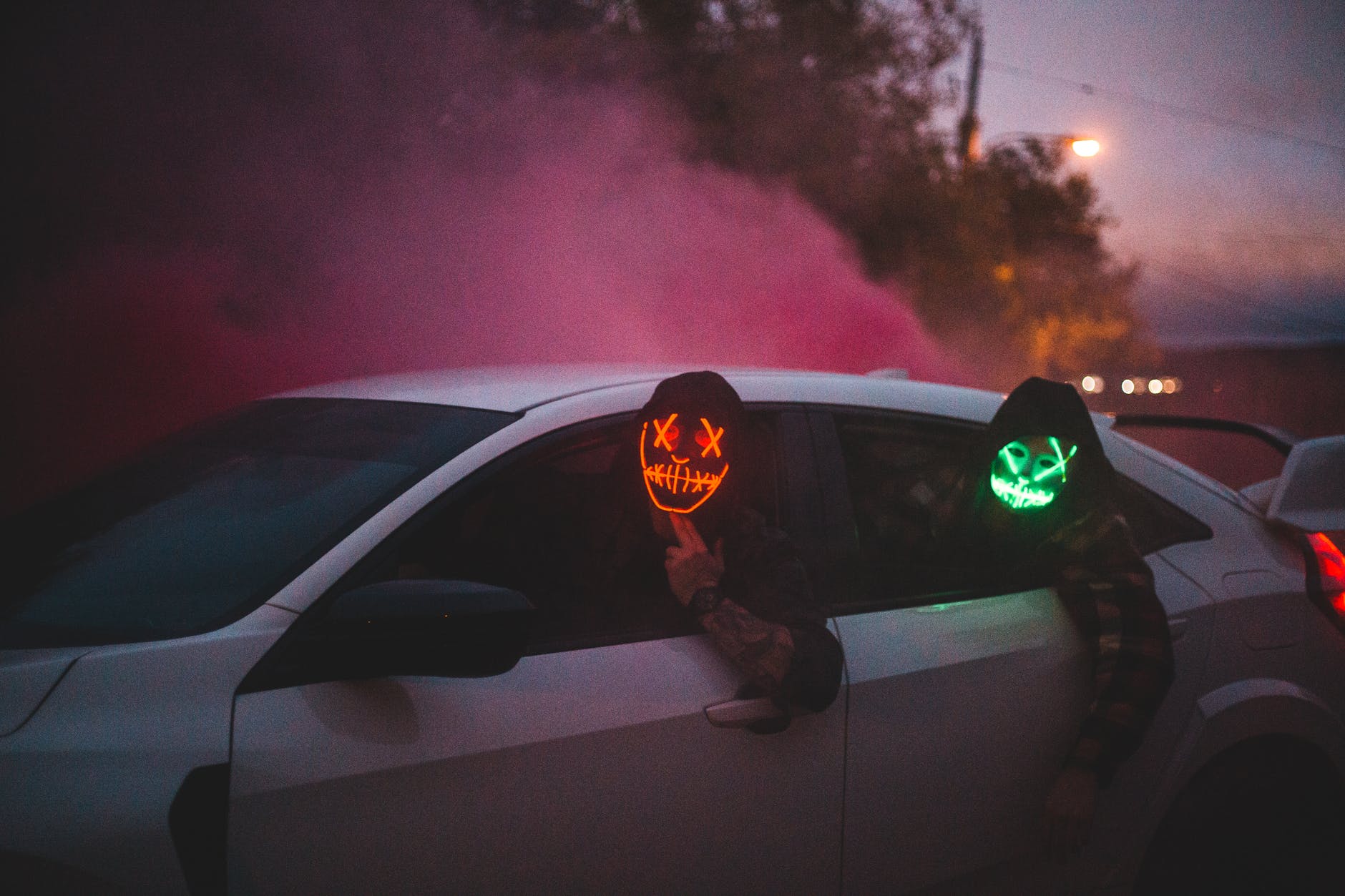 unrecognizable men in glowing halloween masks driving car at night