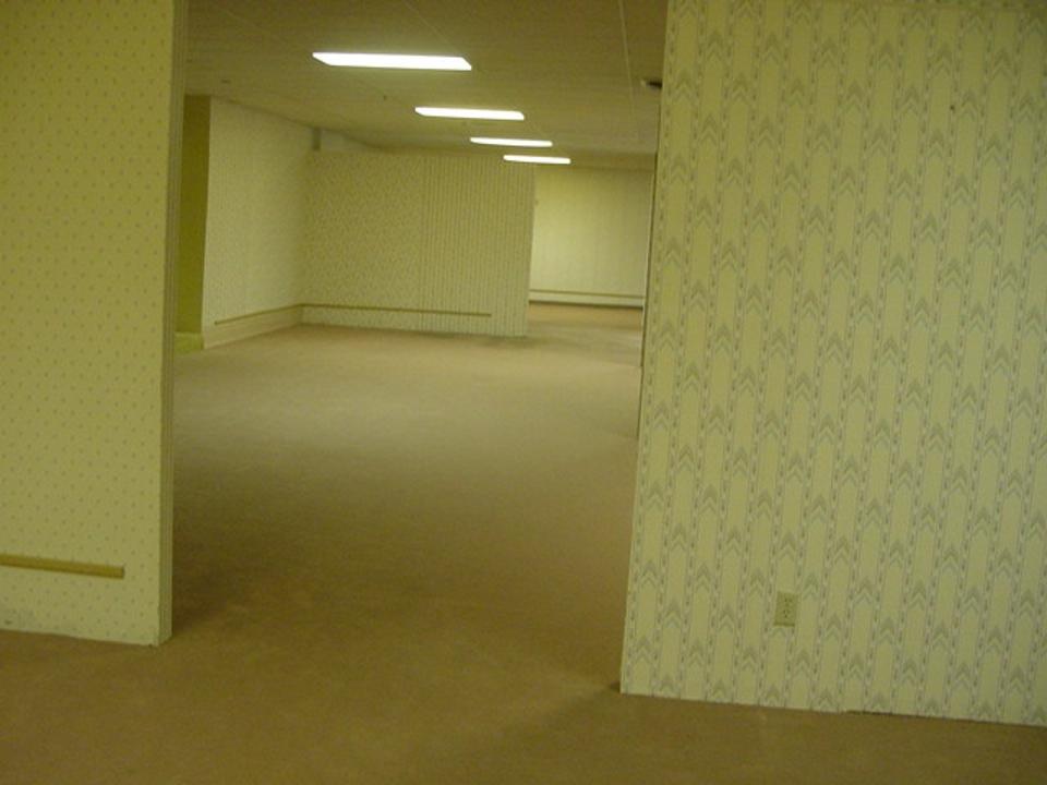 An empty, well-lit room with beige floors and patterned wallpaper, featuring a simple layout and no furnishings.