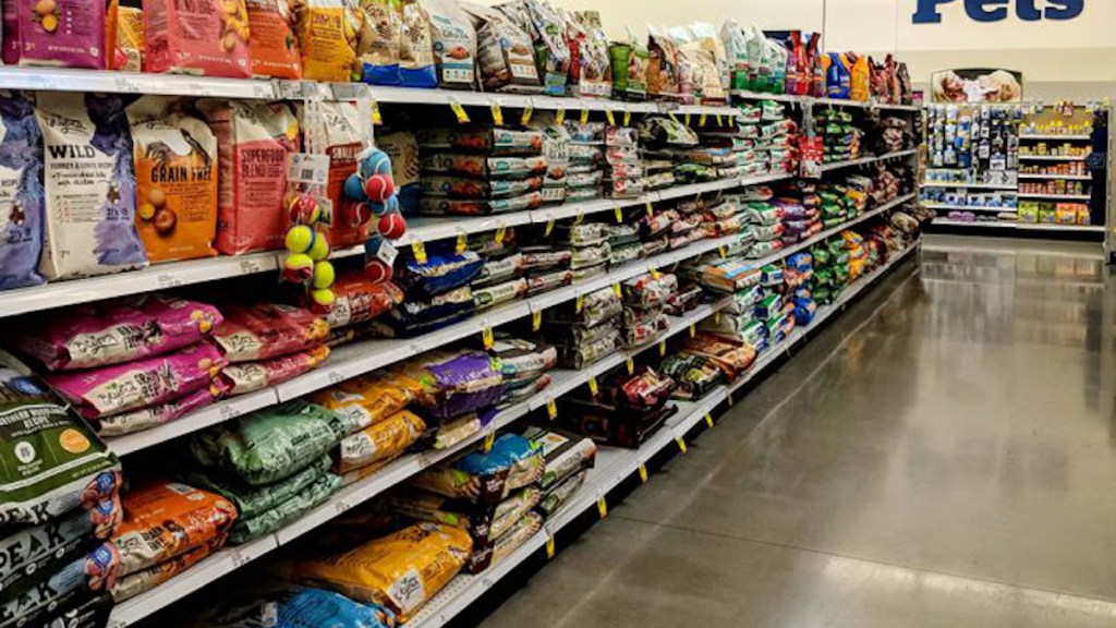 A pet supply aisle featuring various brands of dog and cat food bags on shelves, with colorful packaging and pet toys on display.