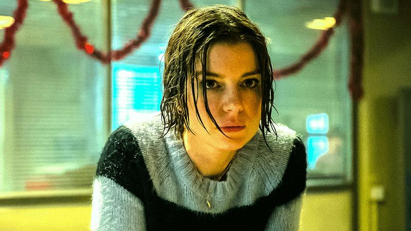 A woman with wet hair staring intently at the camera while wearing a light-colored sweater with black stripes. The background features blurred office elements and holiday decorations.