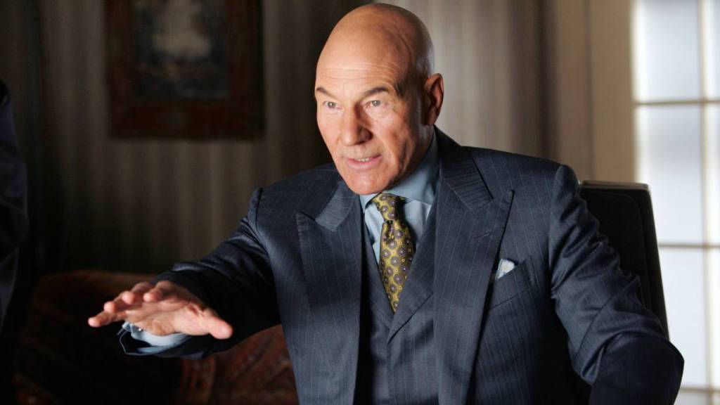 A man in a formal suit gestures confidently while seated at a table, showcasing a professional demeanor in a well-lit office setting.